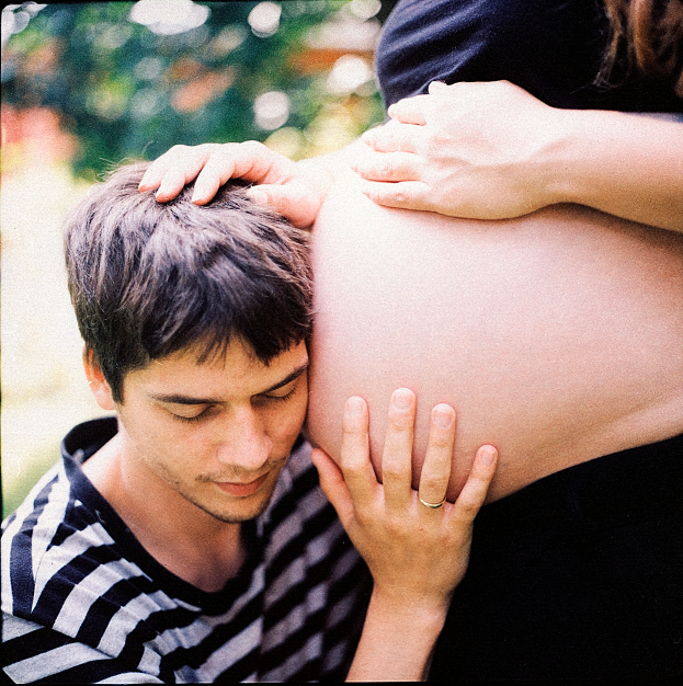 Ein Mann und eine Frau stehen nebeneinander, der Mann berührt sanft den Bauch der Frau, mit einem unscharfen Hintergrund, der das Paar und ihr ungeborenes Kind hervorhebt.