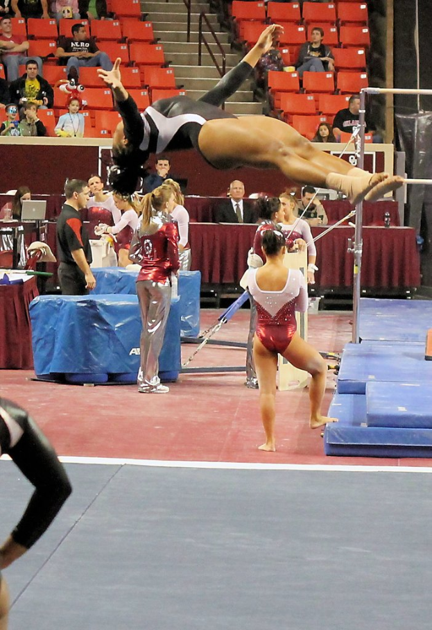 Menschen sitzen in verschiedenen Outfits, eine Person führt in der Mitte Gymnastik aus und es gibt Crashbetten auf der rechten Seite.