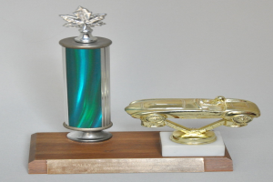 Ein glänzender, fein detaillierter Pokal mit einem Miniaturauto darauf, auf einer hellen Holzplatte montiert.