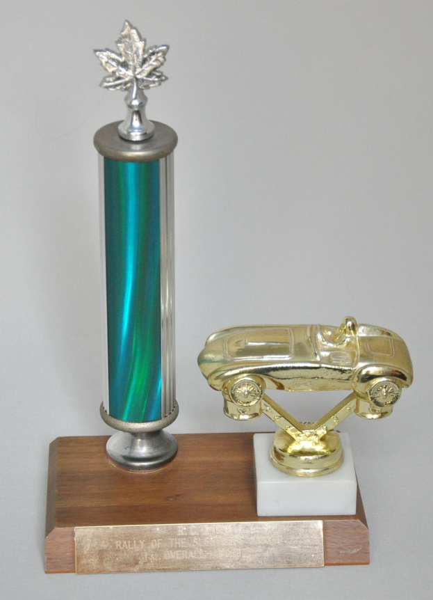 Ein glänzender, fein detaillierter Pokal mit einem Miniaturauto darauf, auf einer hellen Holzplatte montiert.