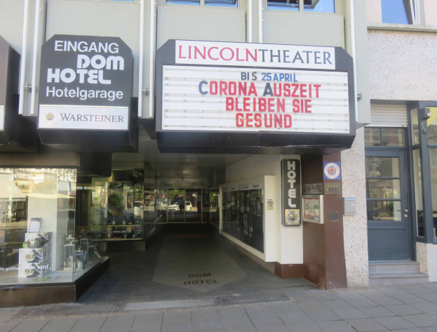 Außenansicht des Lincoln Theaters in Berlin, Deutschland, mit Glasfenstern, Türen und einer Texttafel, mit einem belebten Stadtbild im Inneren.