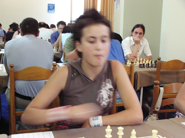 Ein Raum mit Menschen, die an Tischen sitzen und Schach spielen, mit einer Vorhangwand und einem Foto in der Ecke.