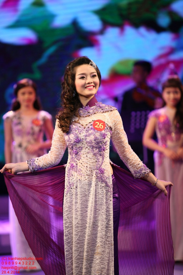 Eine Frau in einem cremefarbenen und lila Kleid mit einem Anstecker daran, mit einem unscharfen Hintergrund.