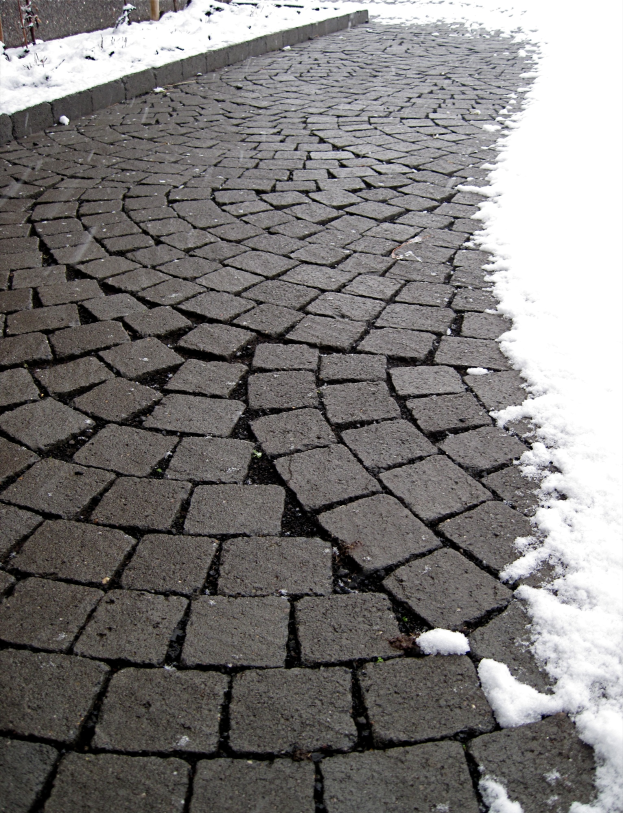 Eine Kopfsteinpflasterstraße mit leichtem Schnee, ein Zaun ist im Hintergrund zu sehen.