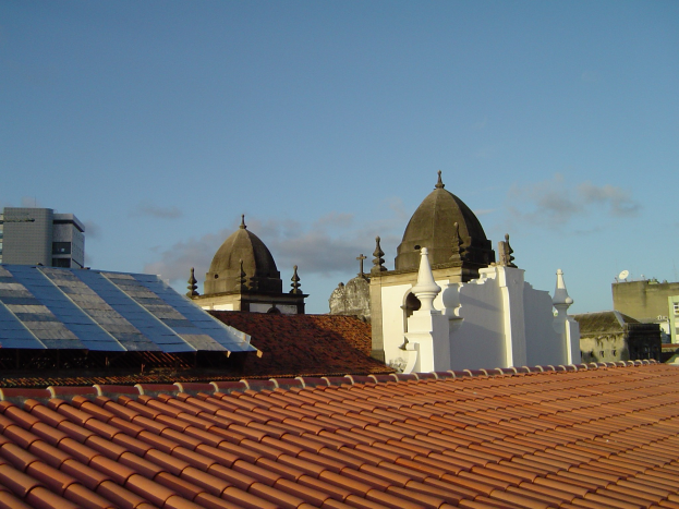 Stadtansicht mit mehreren Gebäuden im Vordergrund, einem klaren blauen Himmel im Hintergrund und Solarpanels auf dem Dach eines Gebäudes.