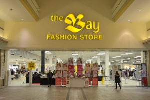 Außenansicht eines Bay Fashion Stores in einem Einkaufszentrum mit Kunden, Wandtafeln, Säulen, Deckenleuchten und Hintergrundauslagen.