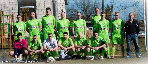 Gruppe von Männern in grünen T-Shirts auf einem Fußballfeld neben einem Torpfosten mit einem Ball davor.
