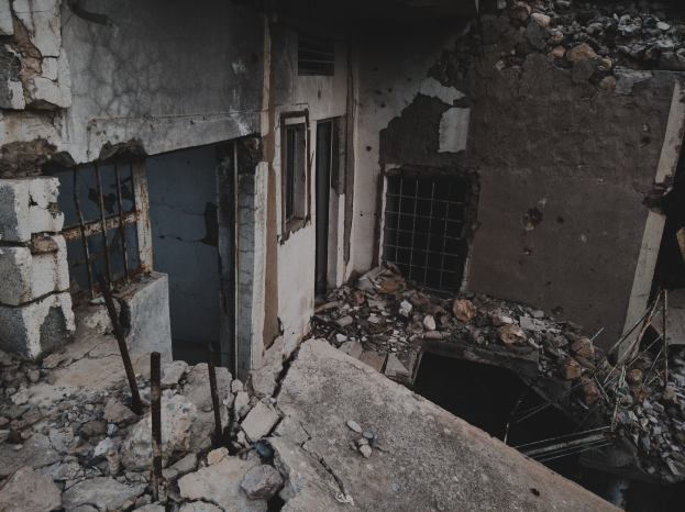 Ein altes, bröckelndes Gebäude mit zerbrochenen Fenstern und herumliegendem Schutt, das einen Zustand des Verfalls und der Vernachlässigung anzeigt.