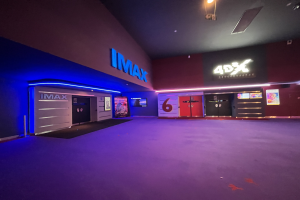 Innenansicht eines Kinos mit lila Teppichboden, Text und Bildschirmen an den Wänden und Deckenbeleuchtung.