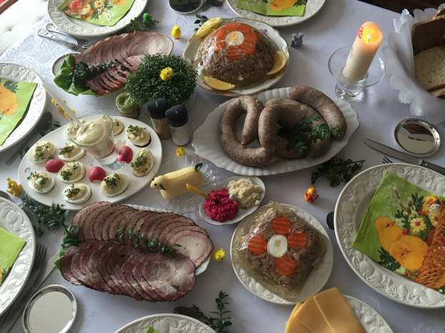 Ein traditioneller deutscher Osterbrunch-Tisch mit verschiedenen Gerichten, Besteck und Kerzen, umgeben von Stühlen.
