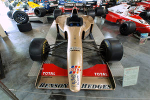 Rennwagen in einem Motorsportmuseum ausgestellt, getrennt von Besuchern und Infotafeln durch einen Metallzaun.