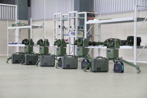 Gruppe von Milit├Ąrrobotern auf einem Boden sitzend mit Koffern und Ausrüstung auf Gestellen, in der N├Ąhe einer Wand und eines Gel├Ąnders als Teil eines Verteidigungs-systems.