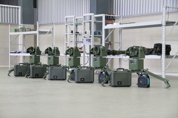 Gruppe von Milit├Ąrrobotern auf einem Boden sitzend mit Koffern und Ausrüstung auf Gestellen, in der N├Ąhe einer Wand und eines Gel├Ąnders als Teil eines Verteidigungs-systems.