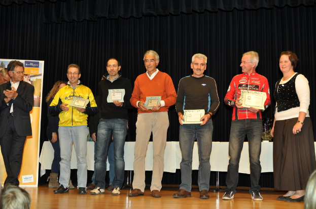 Eine Gruppe von Menschen steht auf einer Bühne und hält Zertifikate in den Händen, mit einem Banner im Hintergrund, einem Tisch daneben und einem schwarzen Vorhang.