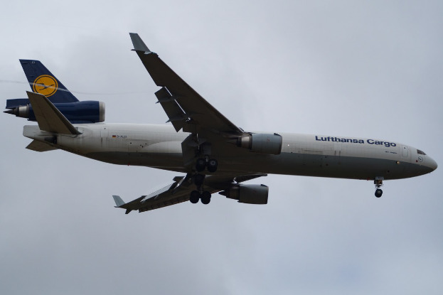 Ein Lufthansa Cargo Boeing 777-300ER im Flug, mit ausgefahrenen Tragflächen und aktivierten Triebwerken, mit sichtbarem Text auf dem Rumpf gegen einen wolkengefüllten Himmel.