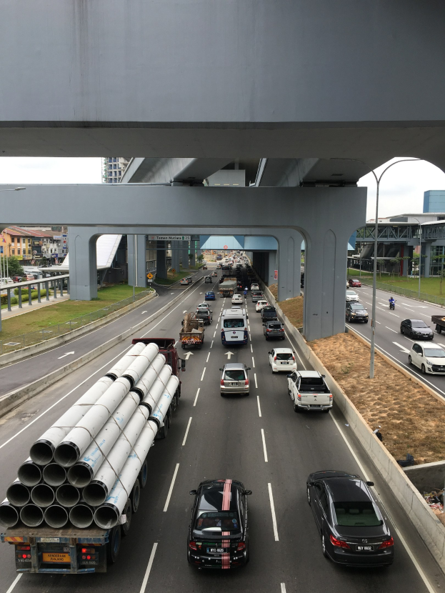 Starker Verkehr auf einer Autobahn unter einer Brücke mit umgebenender Infrastruktur und Vegetation.
