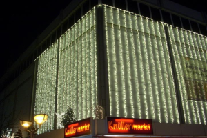 Ein Berliner Gebäude, das mit Weihnachtslichtern geschmückt ist, umgeben von Bäumen, Laternenmasten und Texttafeln, mit dem Himmel im Hintergrund.