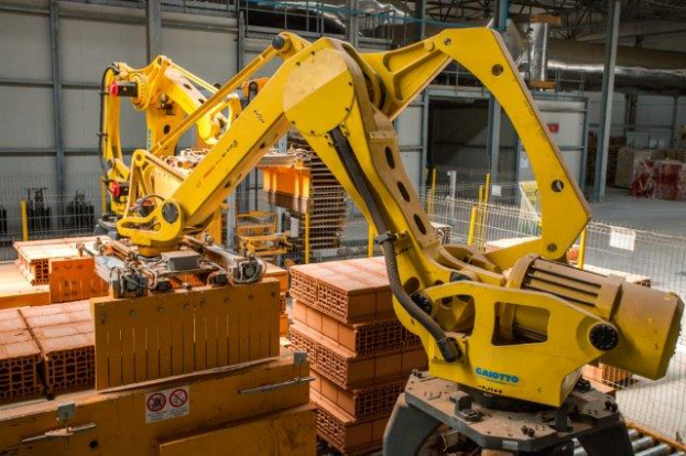 Ein großes Lager voller numerous Kartons, Kräne, einen Zaun, Pfosten und andere industrielle Ausrüstung, mit einer Wand im Hintergrund, die auf eine größere industrielle Anlage hinweist.