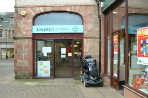 Eine Apothekenfiliale mit einem vor dem Gebäude geparkten Fahrzeug und einem Gebäude in der linken Ecke.