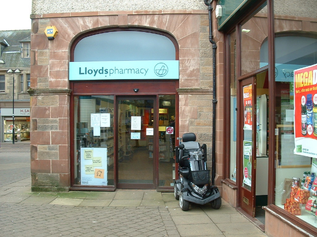 Eine Apothekenfiliale mit einem vor dem Gebäude geparkten Fahrzeug und einem Gebäude in der linken Ecke.