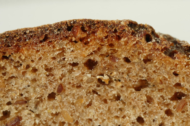 Nahaufnahme eines goldbraunen Roggenbrotlaibs mit leicht knuspriger Kruste und weichem Inneren, mit Rosinen verziert auf einem weißen Teller.