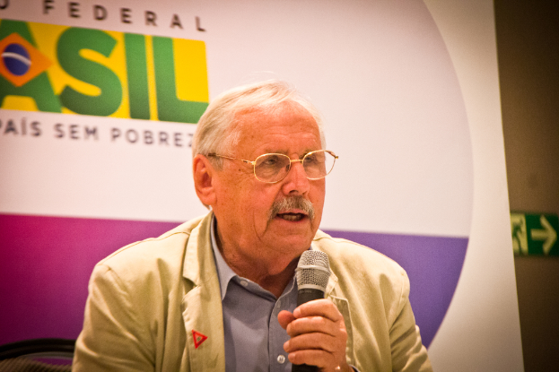 Eine Person, die in ein Mikrofon spricht und ein Banner mit der Aufschrift 'Bundes' hinter sich hat.