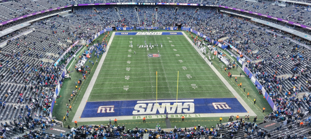 Ein voller Fußballstadion mit Spielern auf dem Feld, Zuschauern auf den Tribünen und Texttafeln am Spielfeldrand.