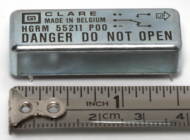 Metallbox mit der Aufschrift "Danger Do Not Open" neben einer Messlatte auf einer weißen Oberfläche.