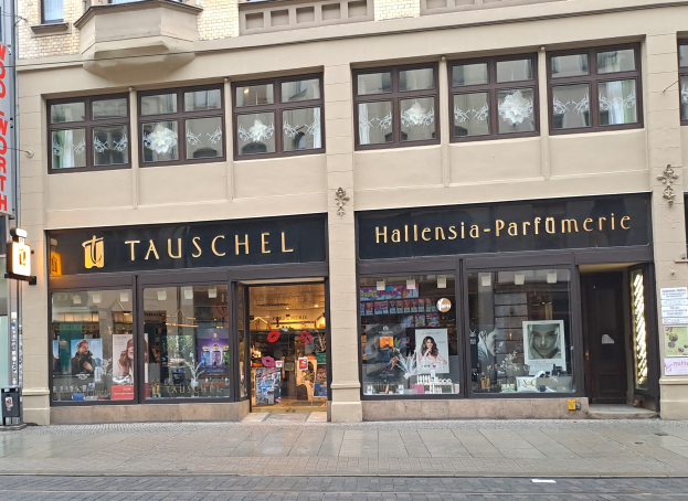Ein Gebäude mit Glaswänden und -fenstern, das Puppen mit Kleidern und anderen Gegenständen zeigt, mit Namensschildern, Plakaten und einem Schild an einem Pfahl draußen, das sich auf einer Straße in Berlin, Deutschland, befindet.